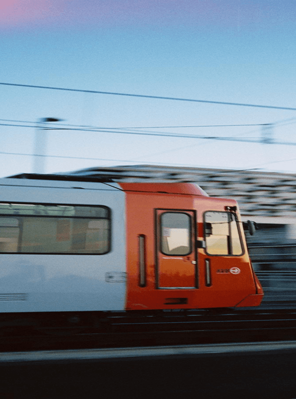 Vista lateral de um trem laranja e branco em alta velocidade com desfoque de movimento.