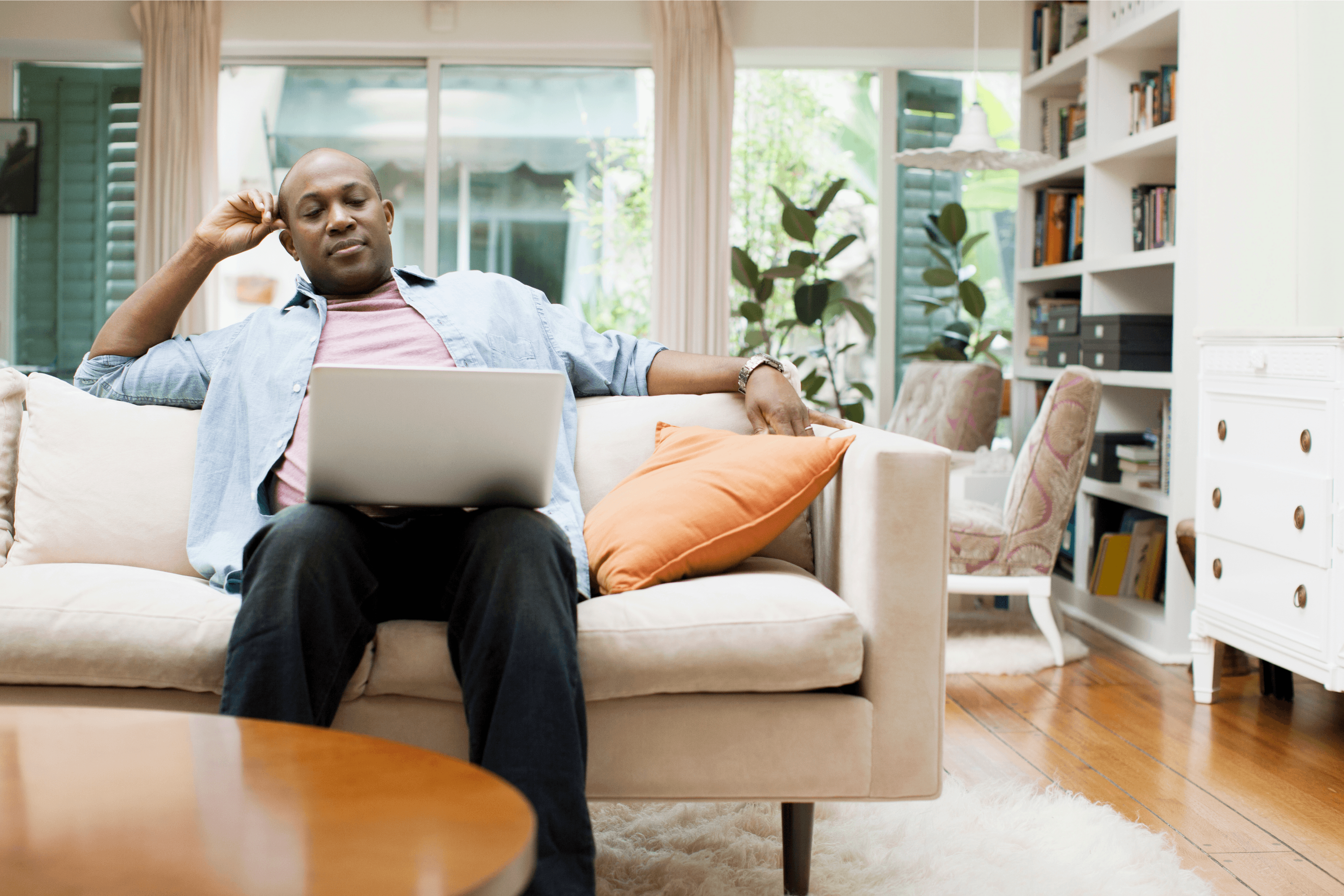 A person sitting on a couch in their home viewing a laptop.