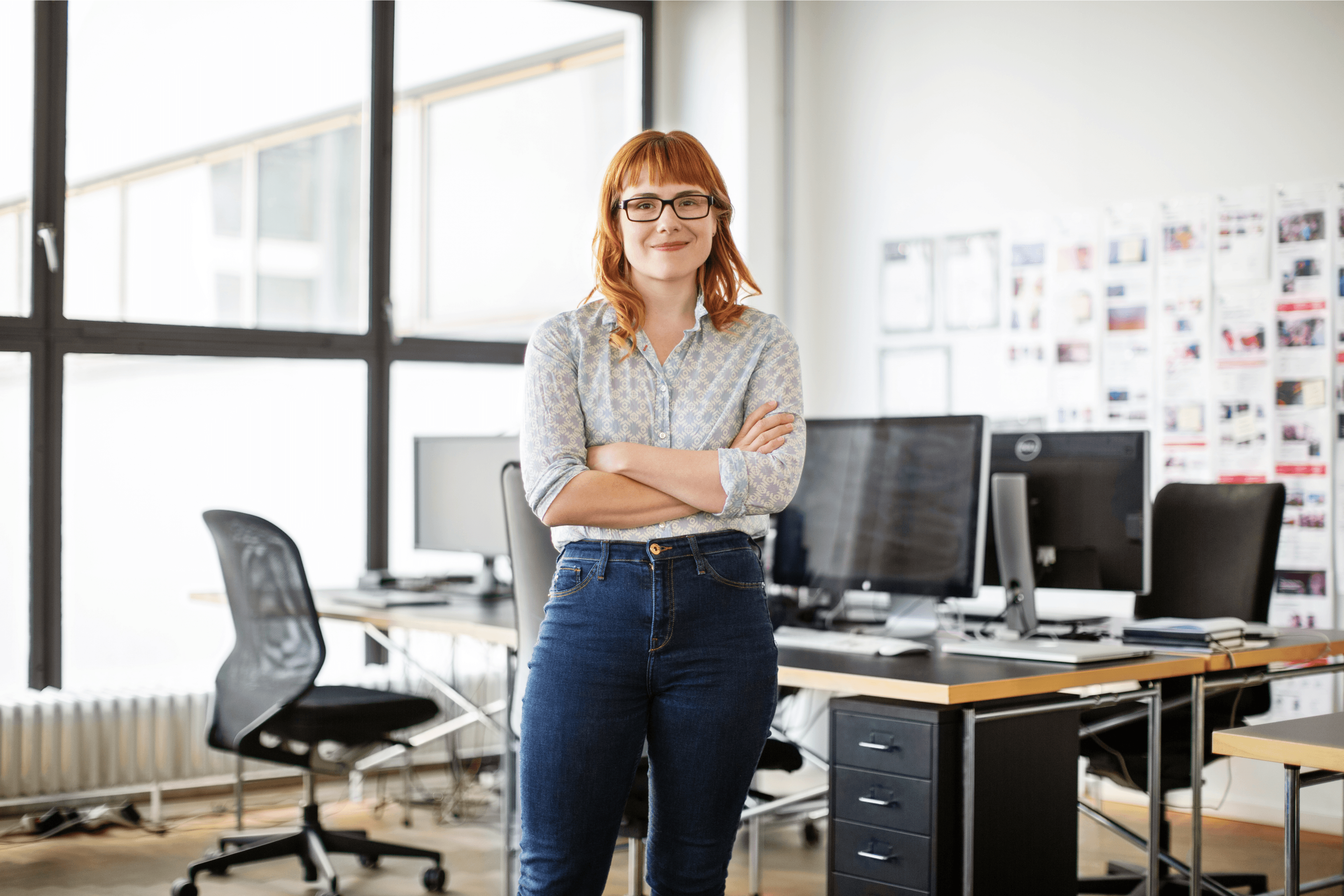 A women standing while crossing her arms and smiling in an office space.
