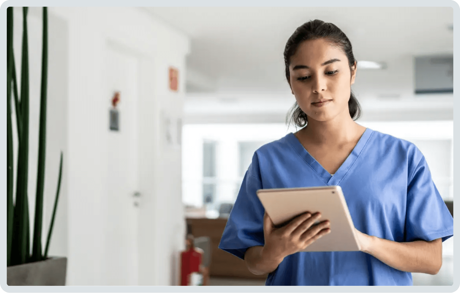 Mulher vestindo uniforme azul olhando para um tablet em um corredor.