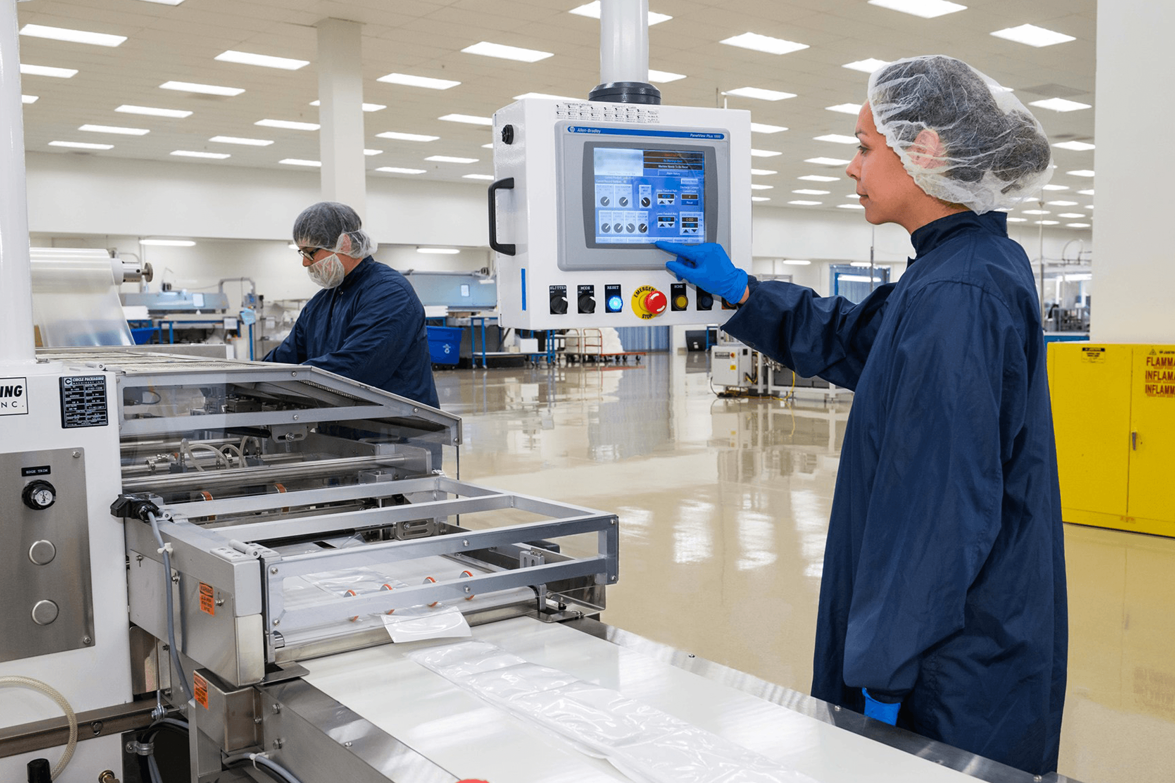 Two cleanroom workers operating sterile packaging machinery.