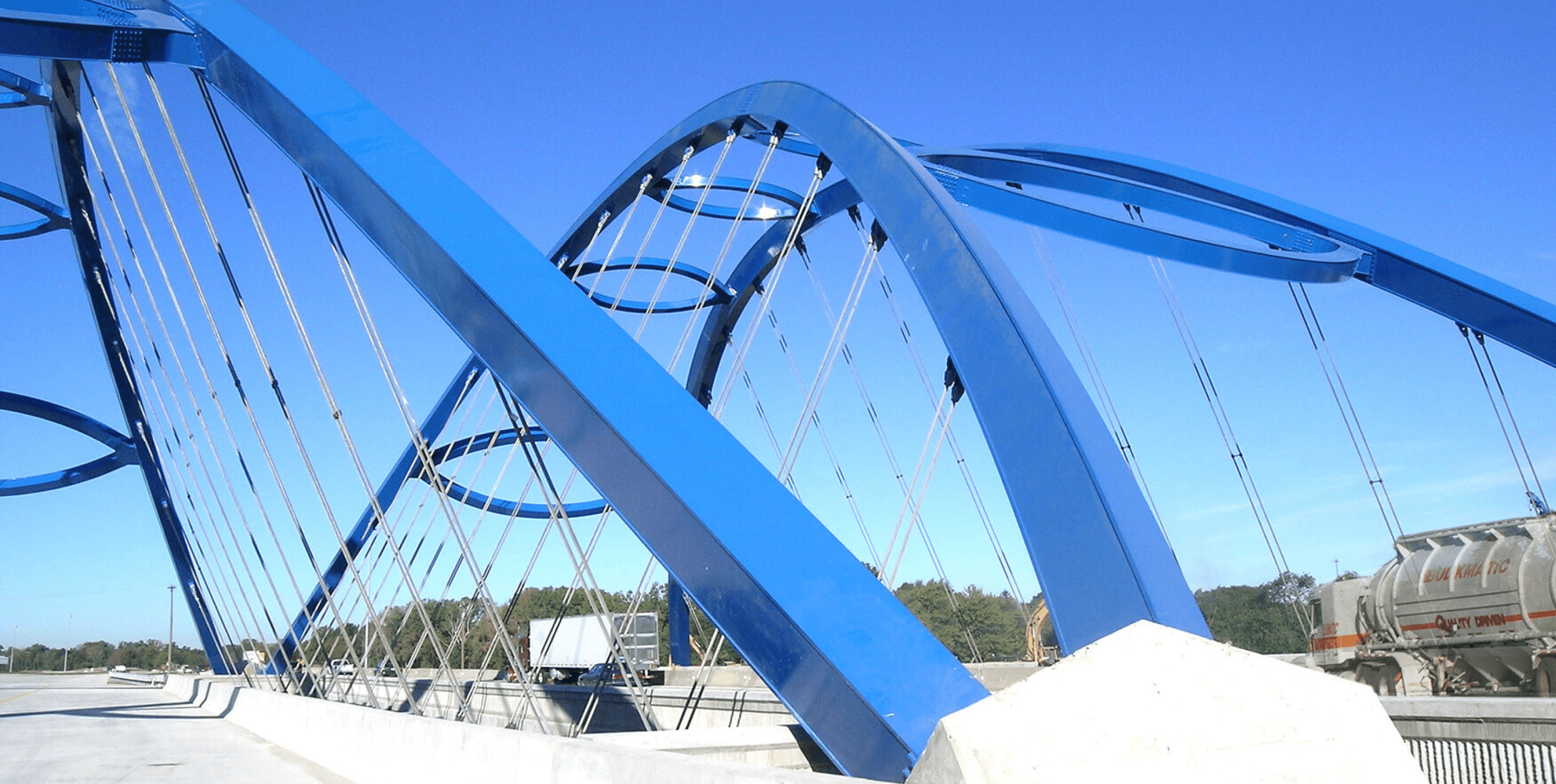 Two blue suspension bridges with commercial trucks passing though.