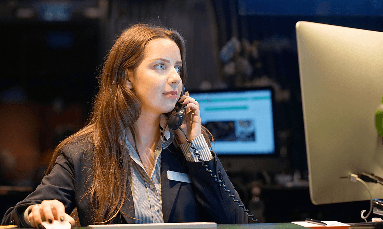 Image of a hotel worker on a phone and working at a computer.