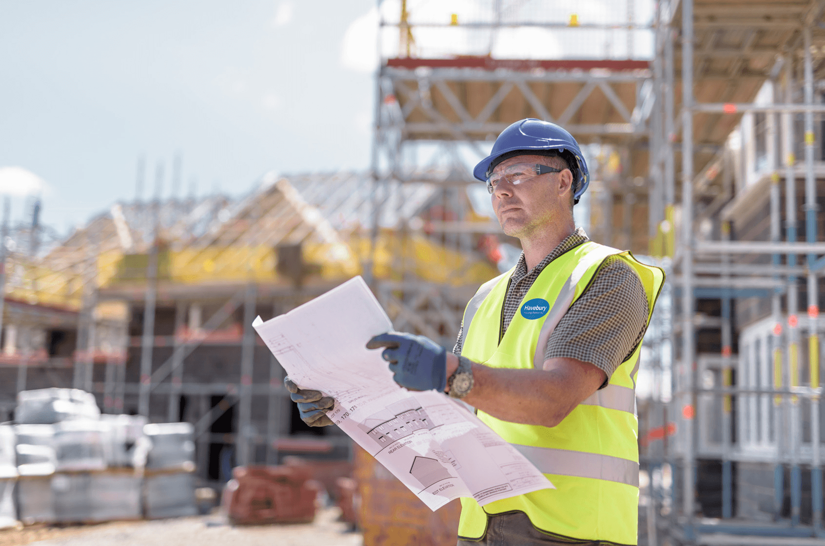A man wearing PPE holds construction plans at a building site.