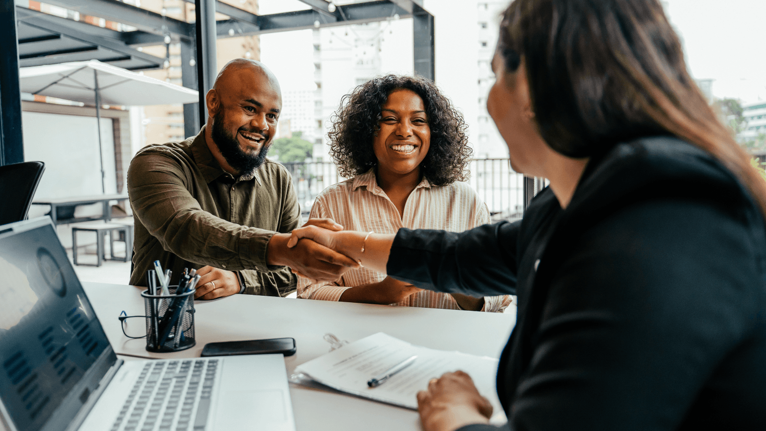 A man and woman smiling while shaking hands with a representative across a table.